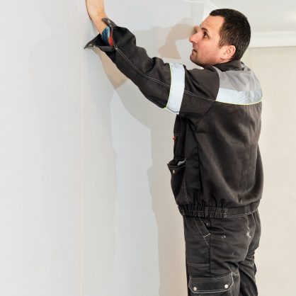 Worker install wallpaper on wall, home restoration concept. Man glues wallpaper on the wall, vertical frame